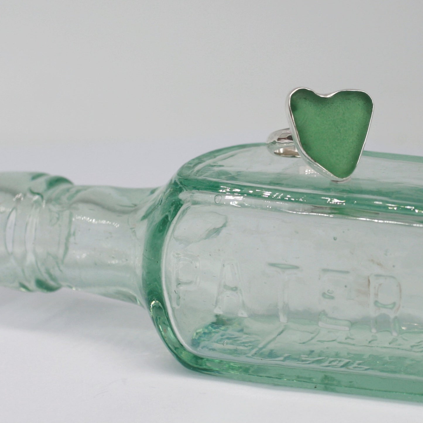 Heart of Green Sea Glass Ring sitting on old glass bottle