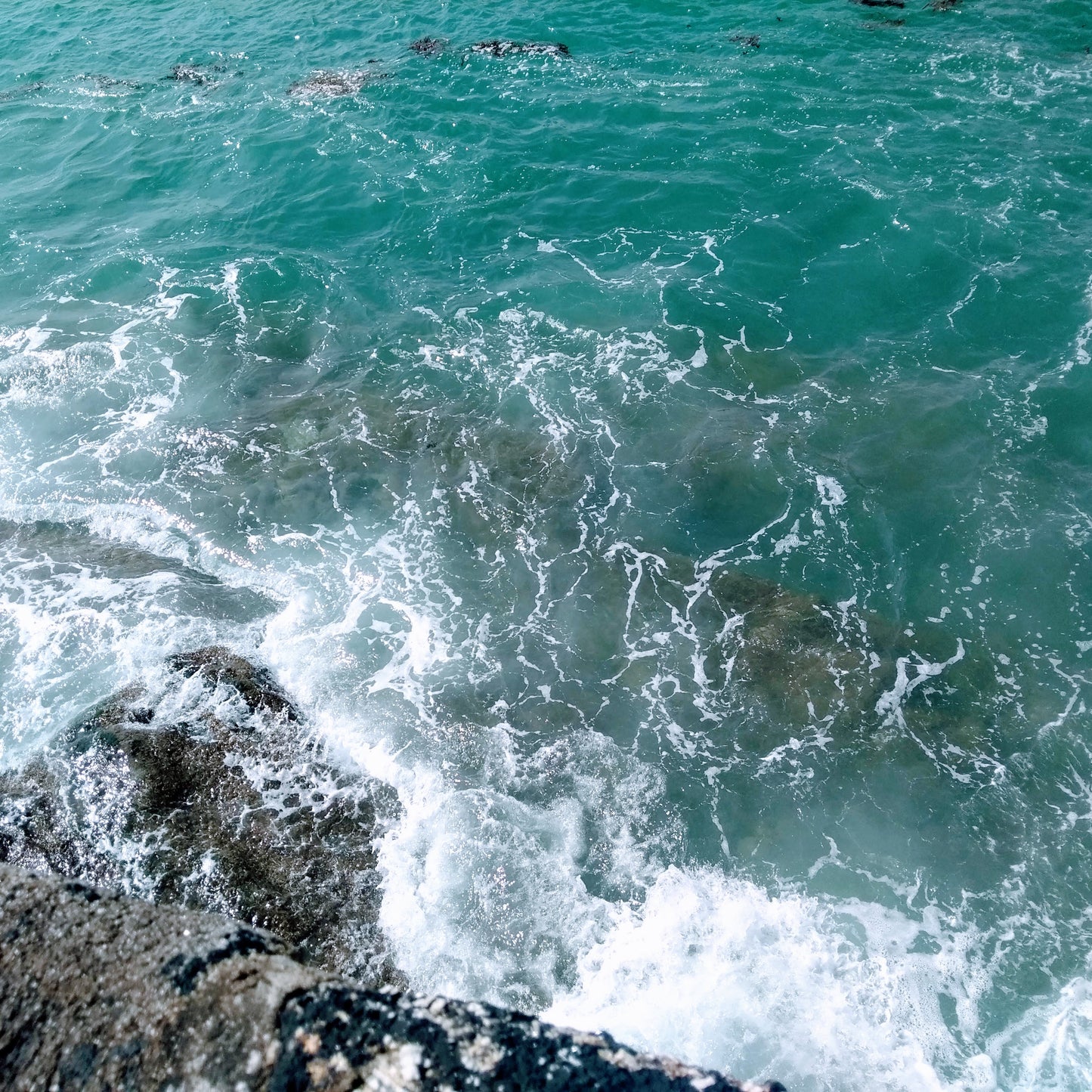Greeny blue sea with seafoam over rocks