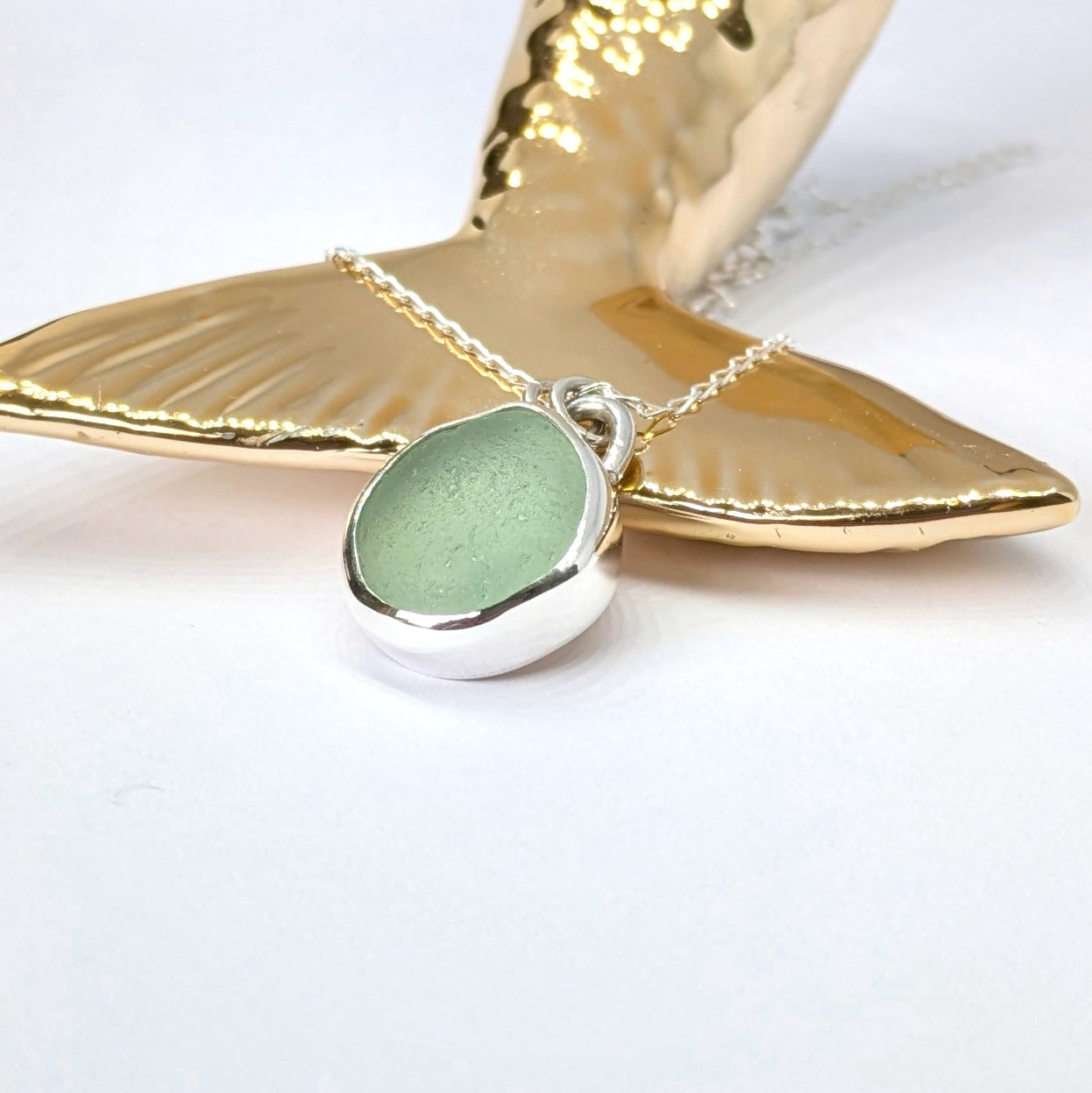 Seafoam sea glass silver pendant resting against gold mermaid type tail
