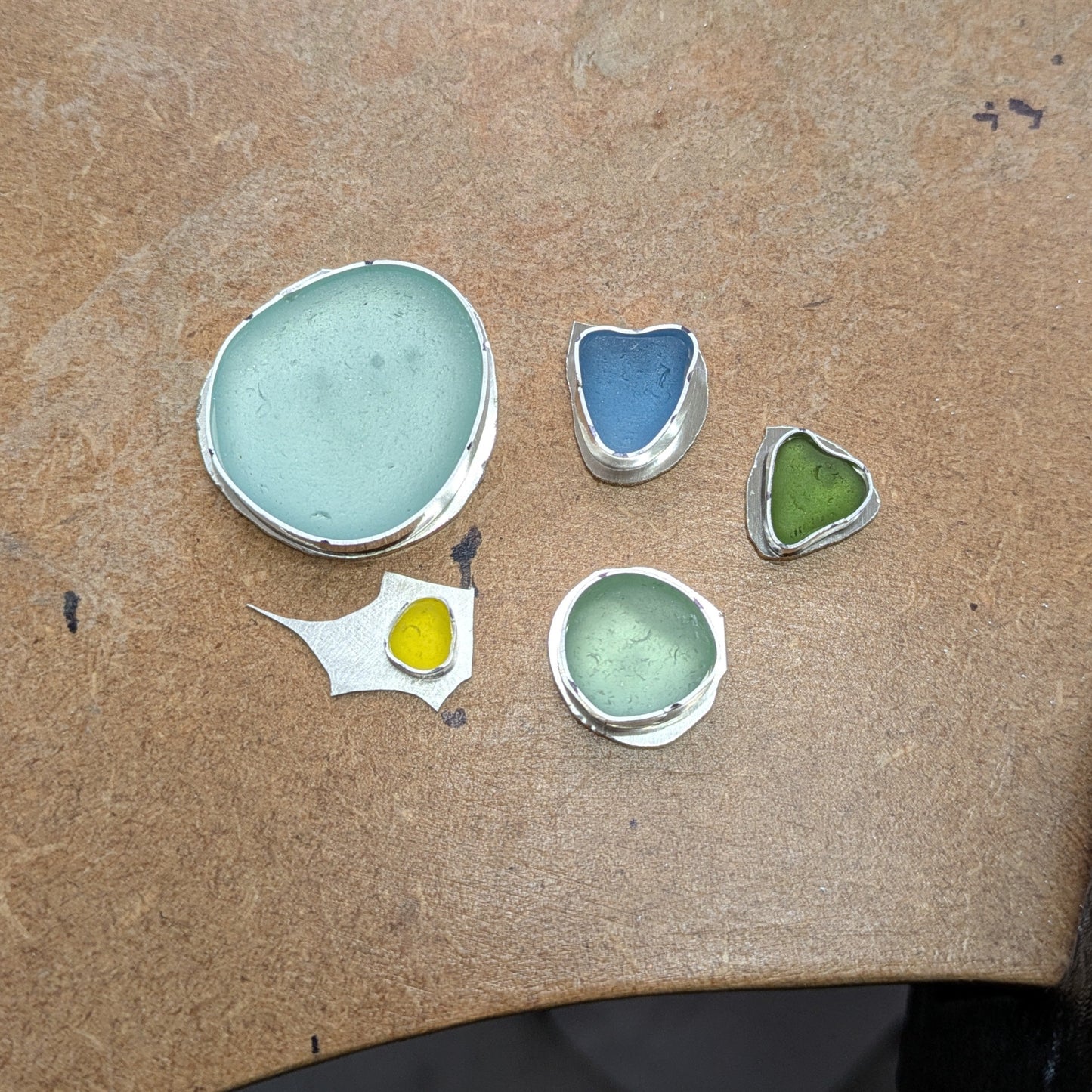 Sea glass sitting in their unfinished silver bezels on workbench