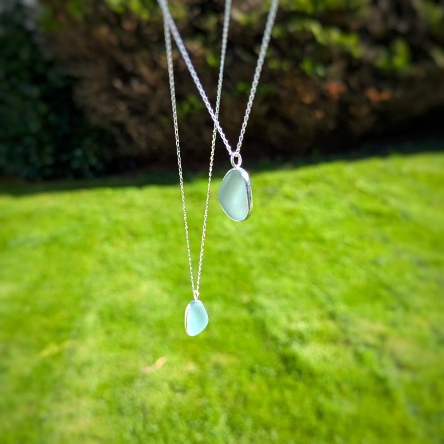 Sea glass pendant in sea foam green set in sterling silver hanging from silver chain, with grass background.
