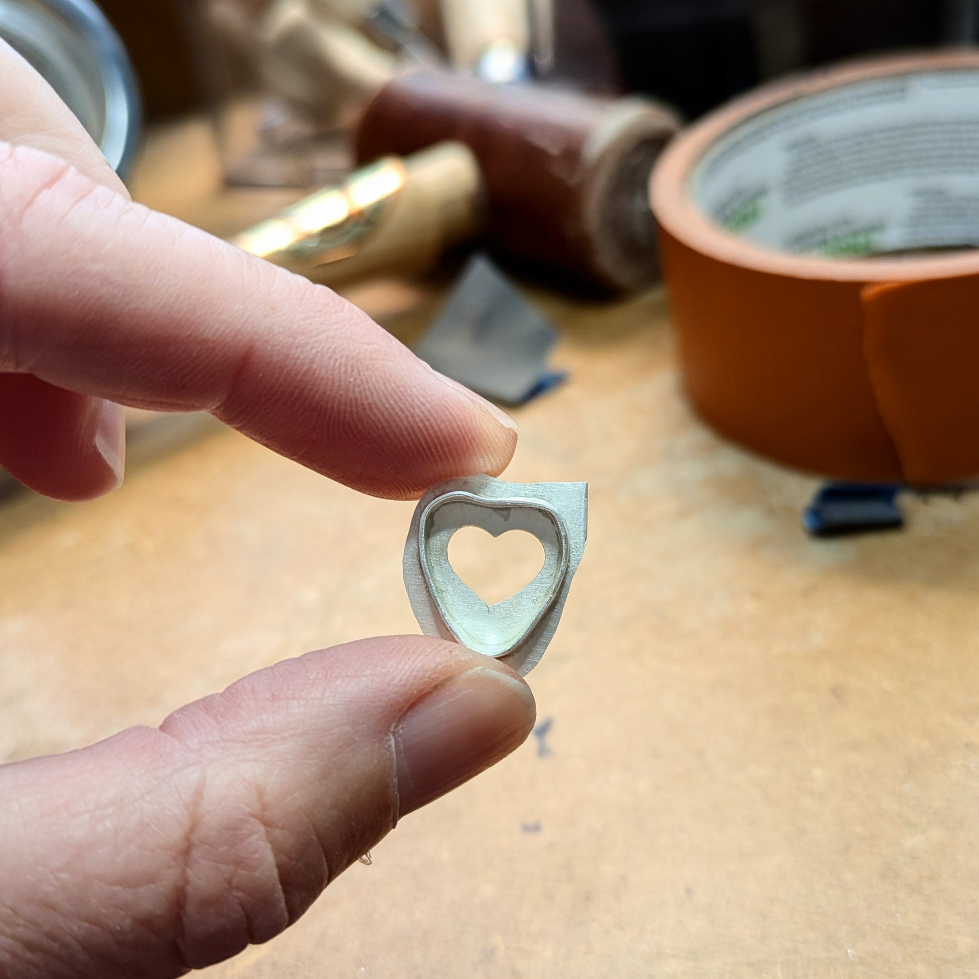 Hand holding silver heart shaped pendant, handmade work in progress