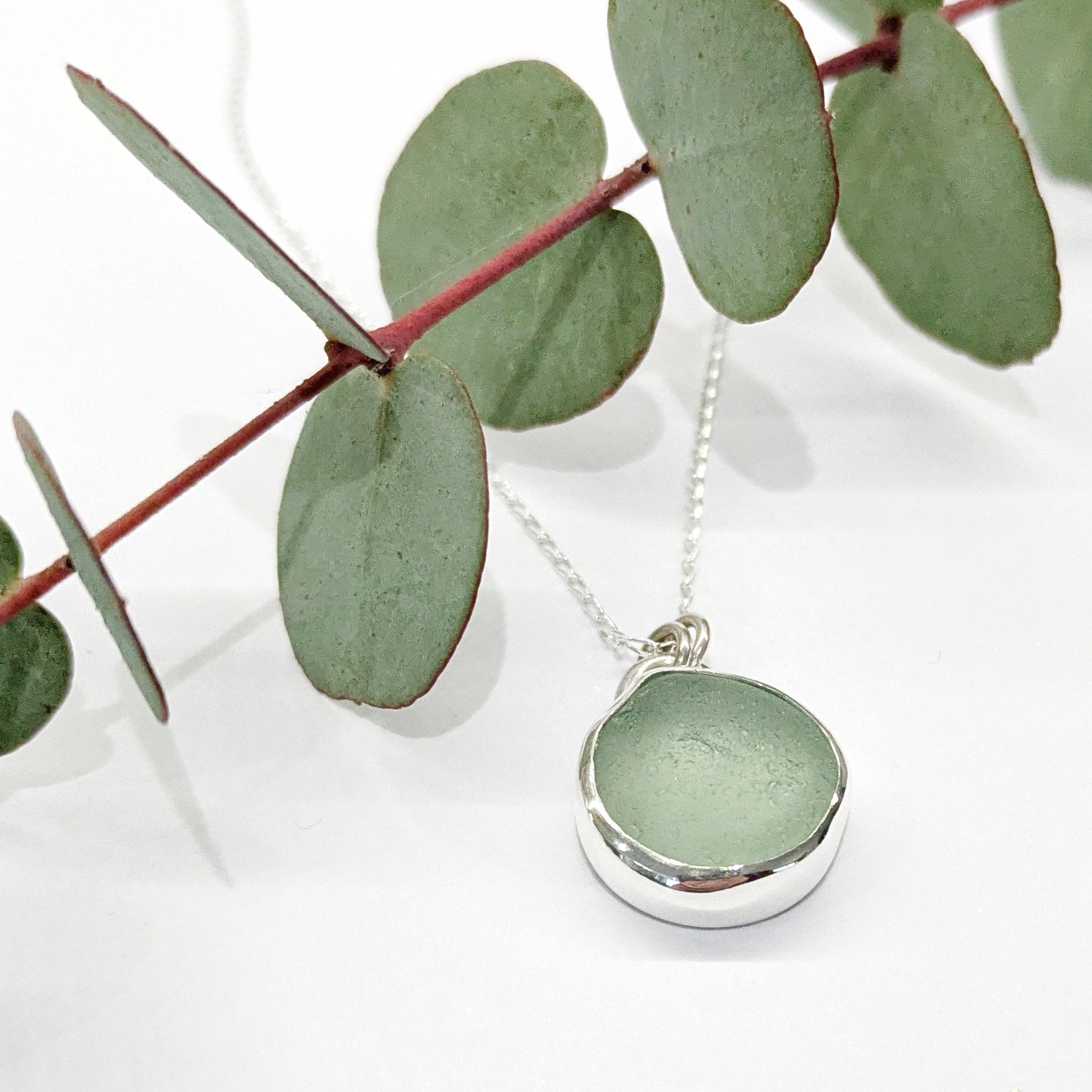 Seafoam sea glass silver pendant on silver chain with festive eucalyptus leaves.
