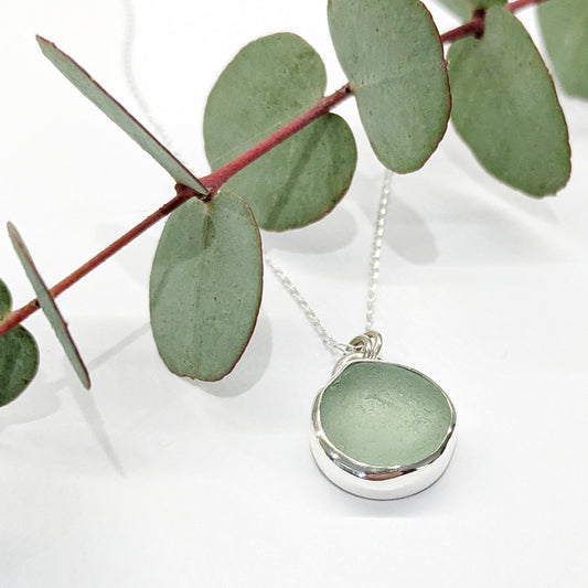 Seafoam sea glass silver pendant on silver chain with festive eucalyptus leaves.