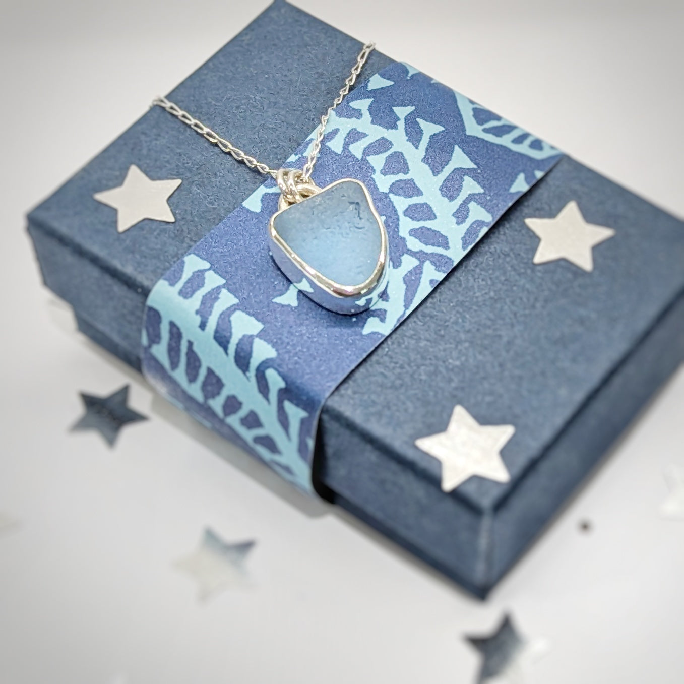 Cornish Blue sea glass silver pendant on silver chain sitting on Nicola Prophet Jewellery Gift box with silver stars.