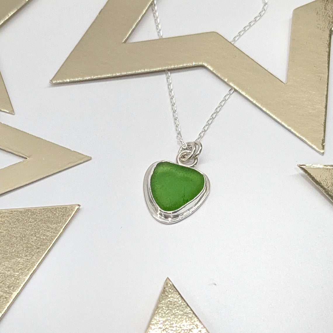 Front of Green Sea Glass silver pendant with heart shape cut out, with silver chain with festive gold star decorations.