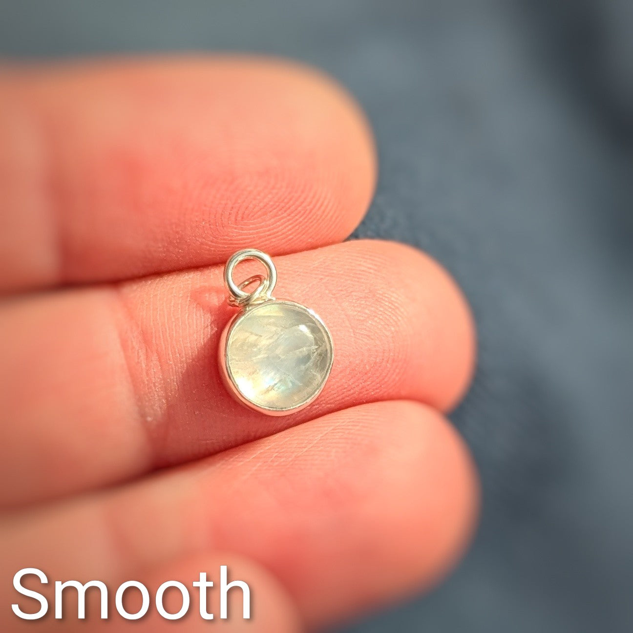 Close up of smooth cut Snowball Moonstone pendant set in sterling silver in hand