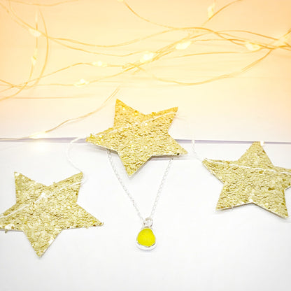 Rare yellow sea glass silver pendant with gold star festive background.