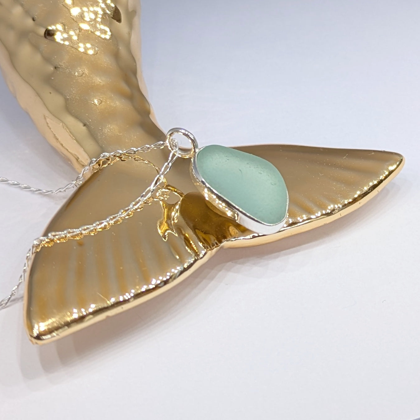 Seafoam sea glass silver pendant sitting on gold mermaid type tail