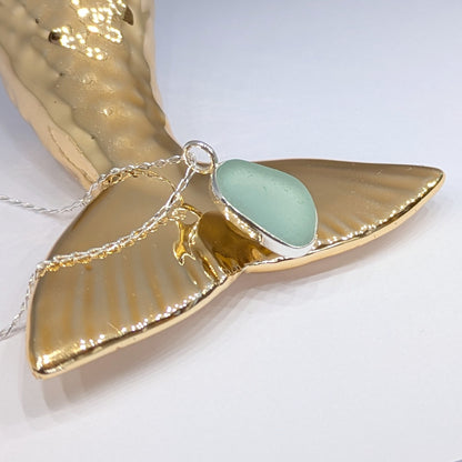 Seafoam sea glass silver pendant sitting on gold mermaid type tail