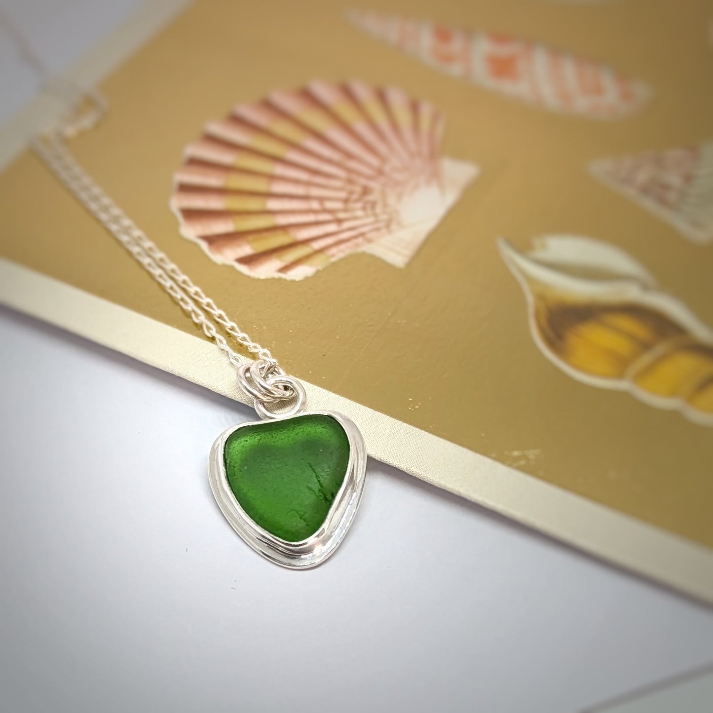 Green Sea Glass silver pendant with heart shape cut out, with silver chain resting on gold shell card