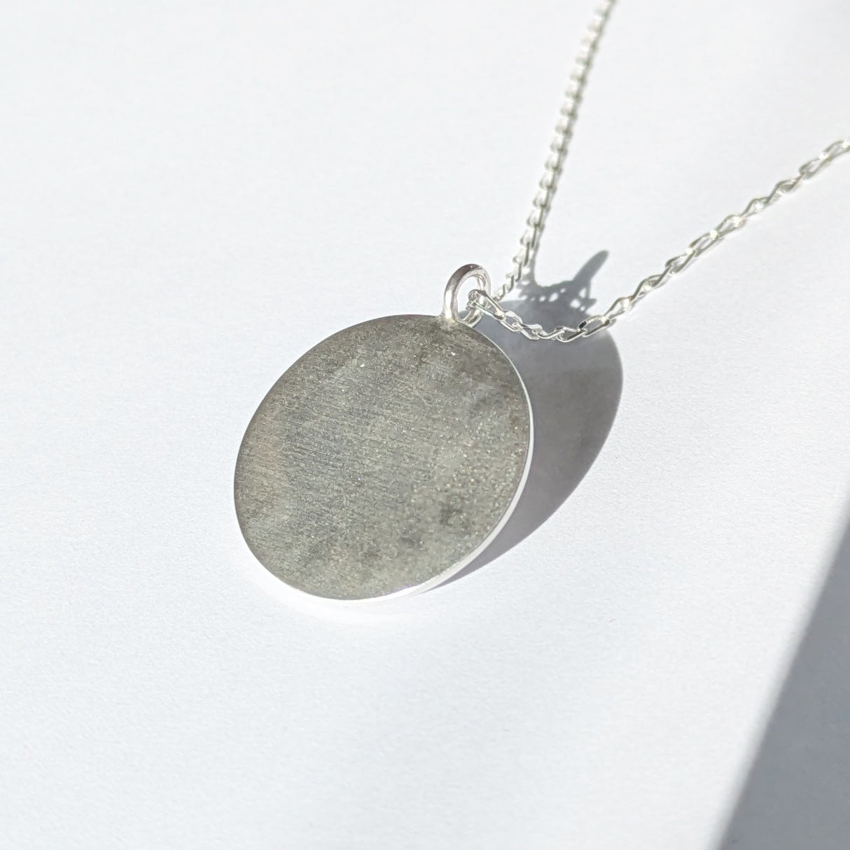 Back of Handmade recycled silver circle pendant, featuring the words ' Shine Bright' around a central golden citrine gemstone. 