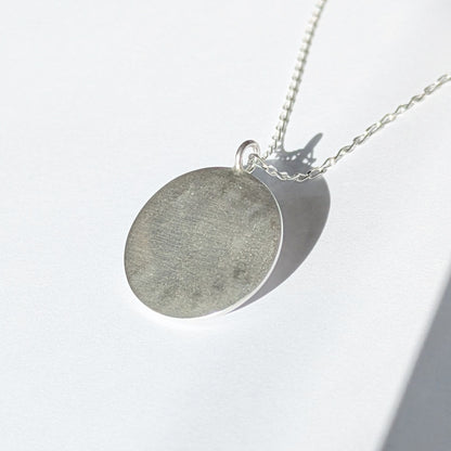 Back of Handmade recycled silver circle pendant, featuring the words ' Shine Bright' around a central golden citrine gemstone. 