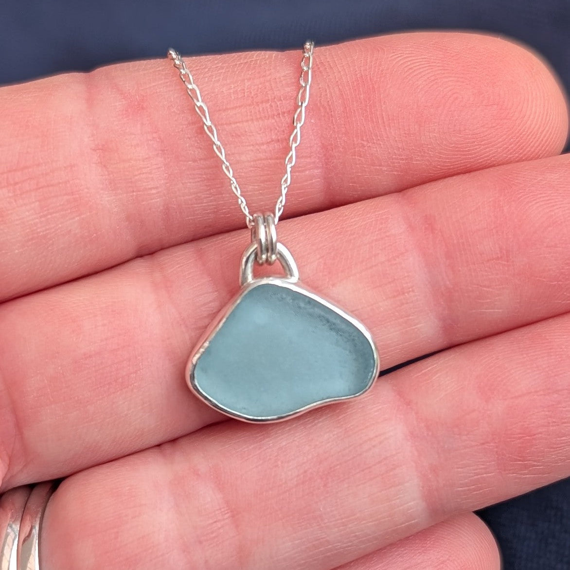 Pale Blue Cornish Sea Glass set in recycled silver with silver chain sitting in hand