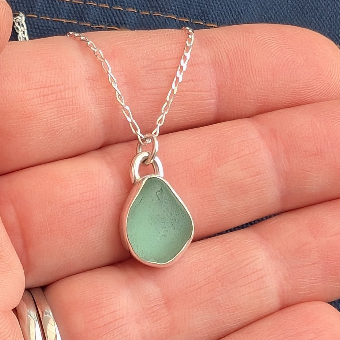 Seafoam Cornish sea glass and silver drop pendant necklace on silver chain in hand