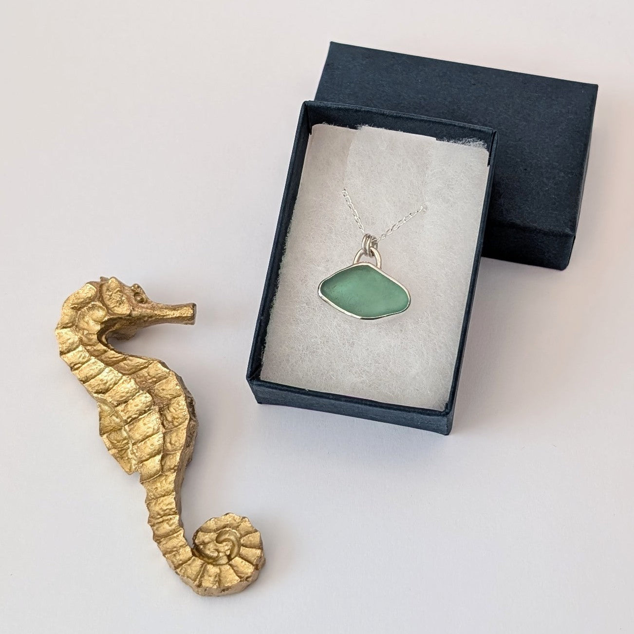 Soft Aqua Cornish sea glass and silver pendant necklace on silver chain in a blue gift box next to golden  sea horse
