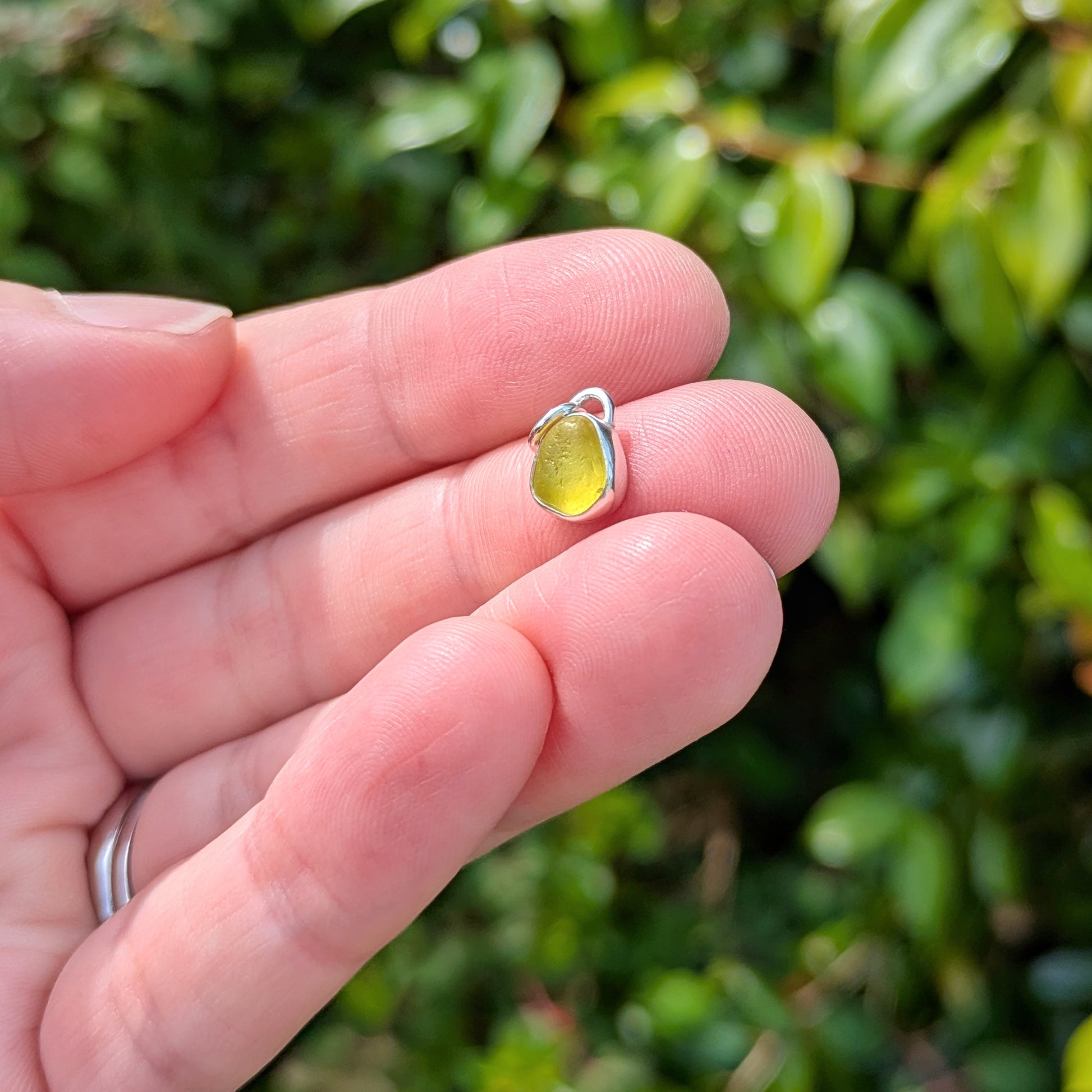 Hand holding Rare yellow sea glass silver pendant outside