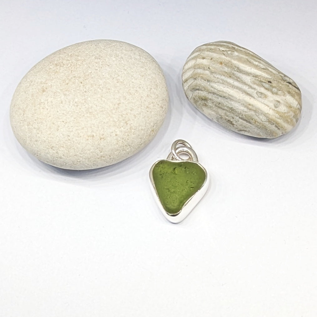 St Ives Green sea glass silver pendant with heart cut out next to pebbles