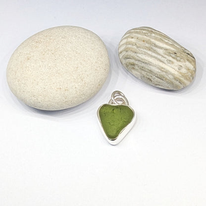 St Ives Green sea glass silver pendant with heart cut out next to pebbles