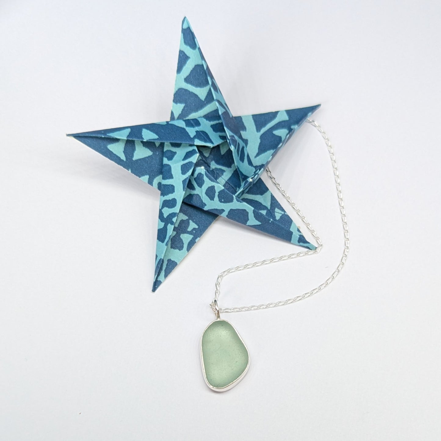 Blue origami star next to Seafoam sea glass silver pendant