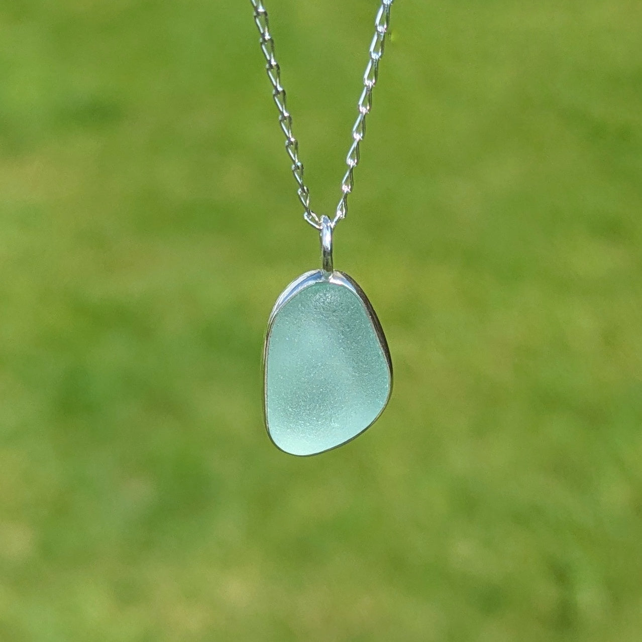 Seafoam sea glass silver pendant hanging from chain outside