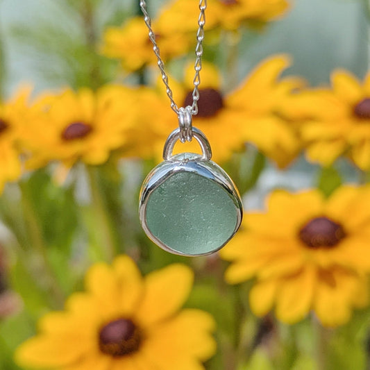 Seafoam sea glass silver pendant with yellow flowers in background