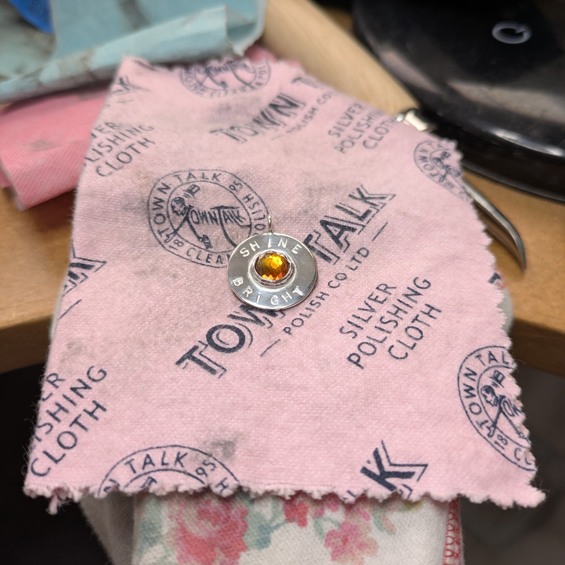 Handmade recycled silver circle pendant, featuring the words ' Shine Bright' around a central golden citrine gemstone.  Pictured on a pink polishing cloth.
