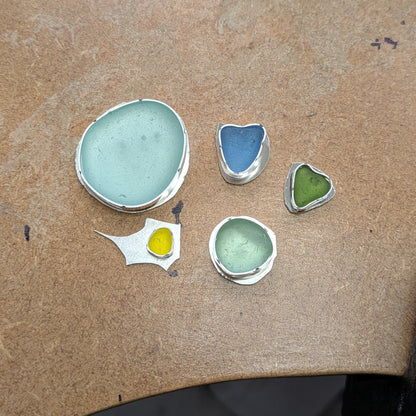Sea glass sitting in their unfinished silver bezels on workbench