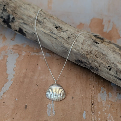 Pure Silver sea shell pendant cast from a real sea shell next to beach driftwood