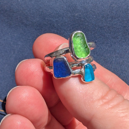 Hand holding three Cornish sea glass hammered silver rings in turquoise, green and blue