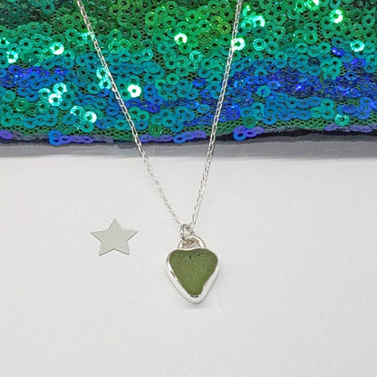 Front of St Ives Green sea glass silver pendant with heart shaped cut out on silver chain, with festive background.