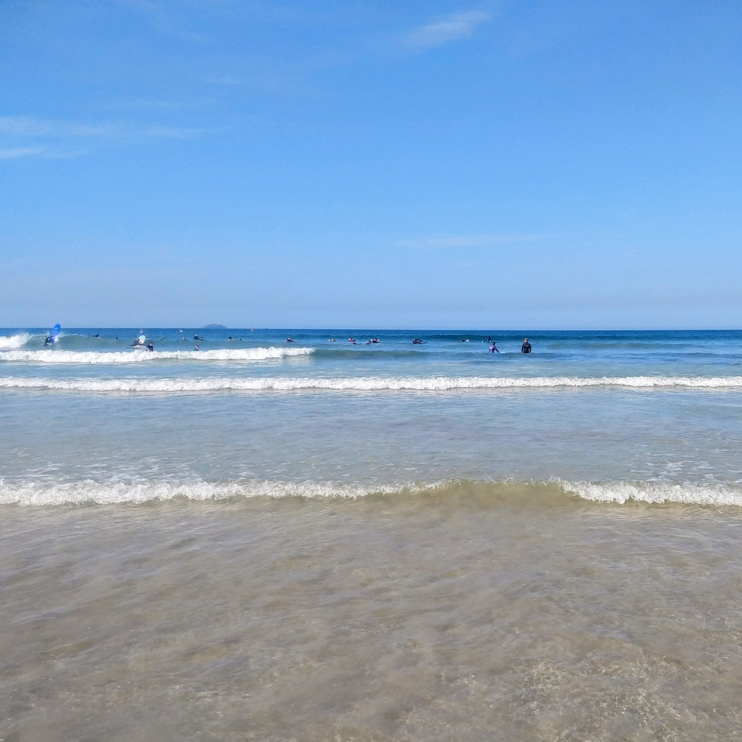 Sunny day at Polzeath beach, Cornwall, with surfers in the sea.