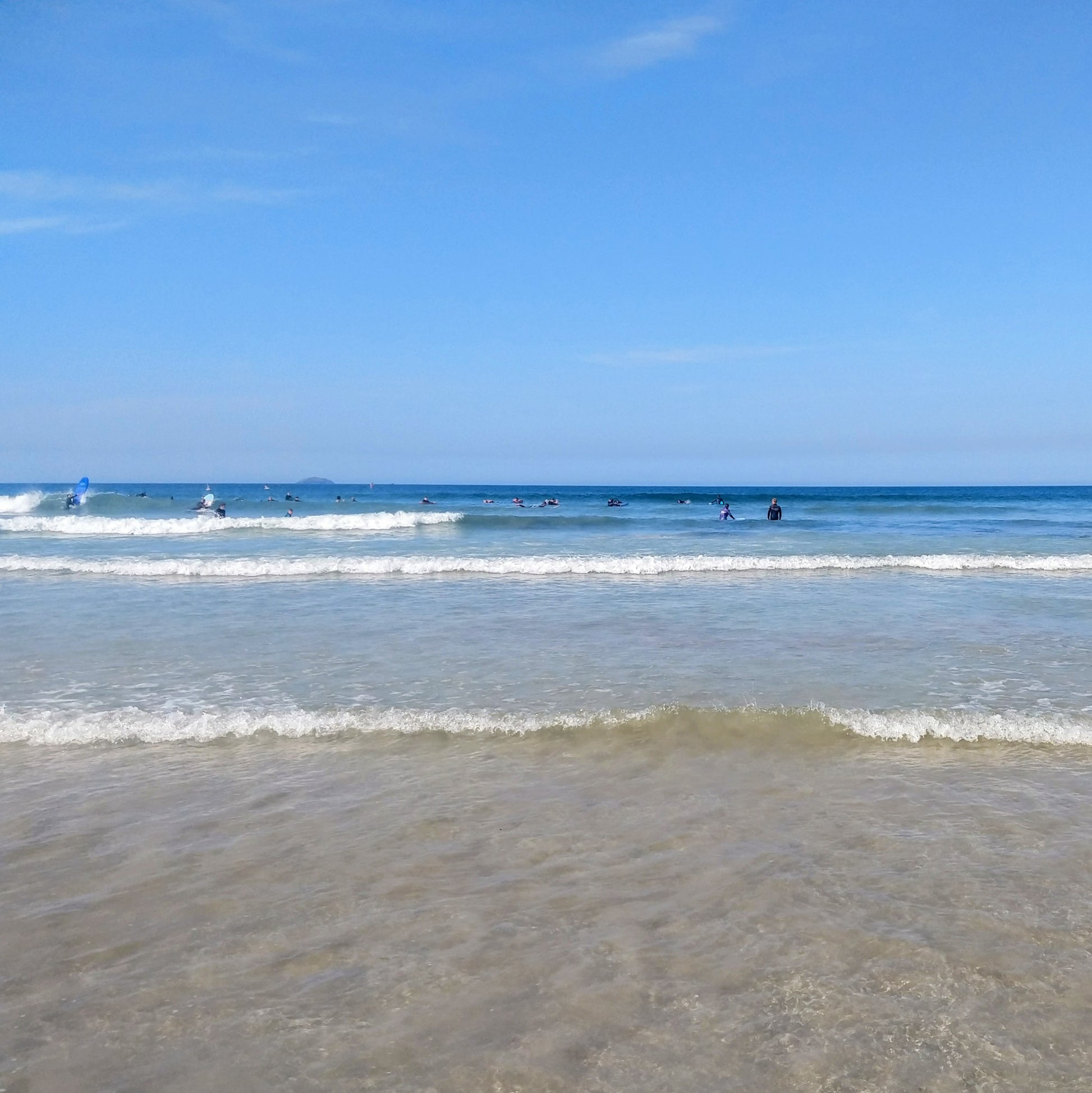 Sunny day at Polzeath beach, Cornwall, with surfers in the sea.