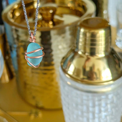 Turquoise sea glass wrapped in copper pendant, set against a golden cocktail background