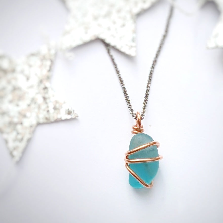 Turquoise sea glass wrapped in copper pendant with silver stars in background
