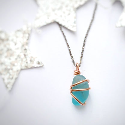 Turquoise sea glass wrapped in copper pendant with silver stars in background