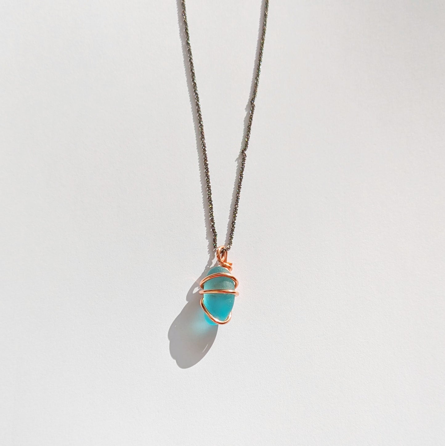 Turquoise sea glass wrapped in copper pendant with white background