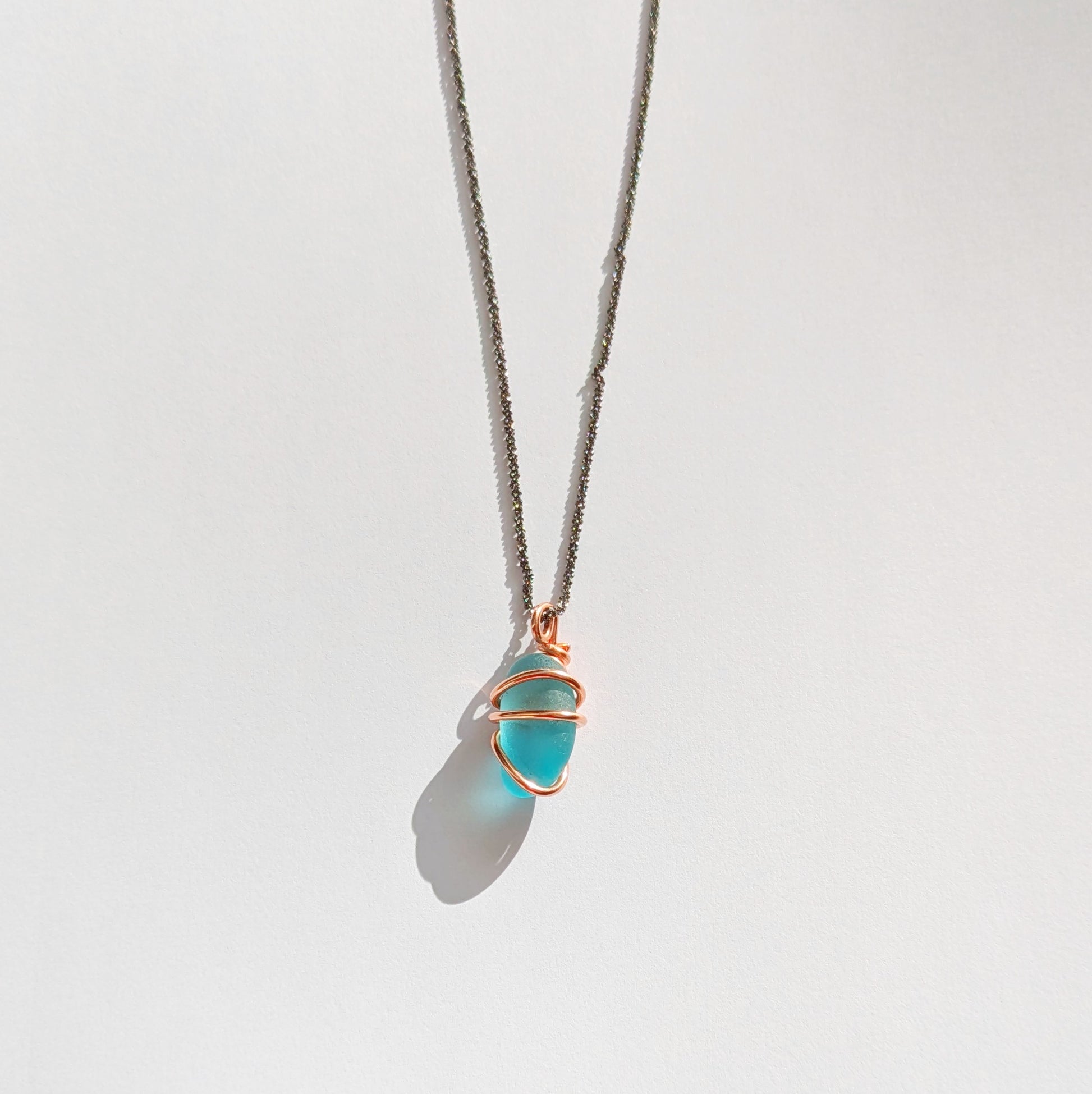 Turquoise sea glass wrapped in copper pendant with white background
