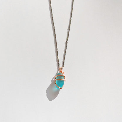 Turquoise sea glass wrapped in copper pendant with white background