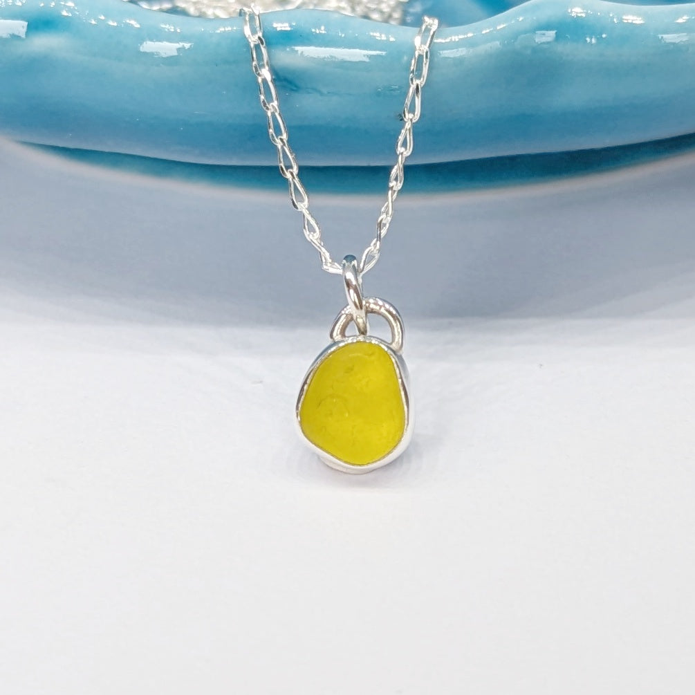 Rare yellow sea glass silver pendant on chain hanging from blue dish