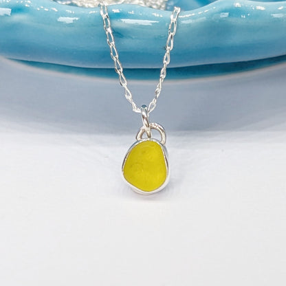 Rare yellow sea glass silver pendant on chain hanging from blue dish