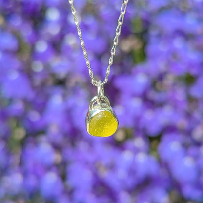Rare yellow sea glass silver pendant in front of purple flowers