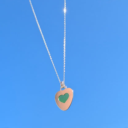 Green Sea Glass silver pendant with heart shape cut out, with silver chain held up to blue sky.