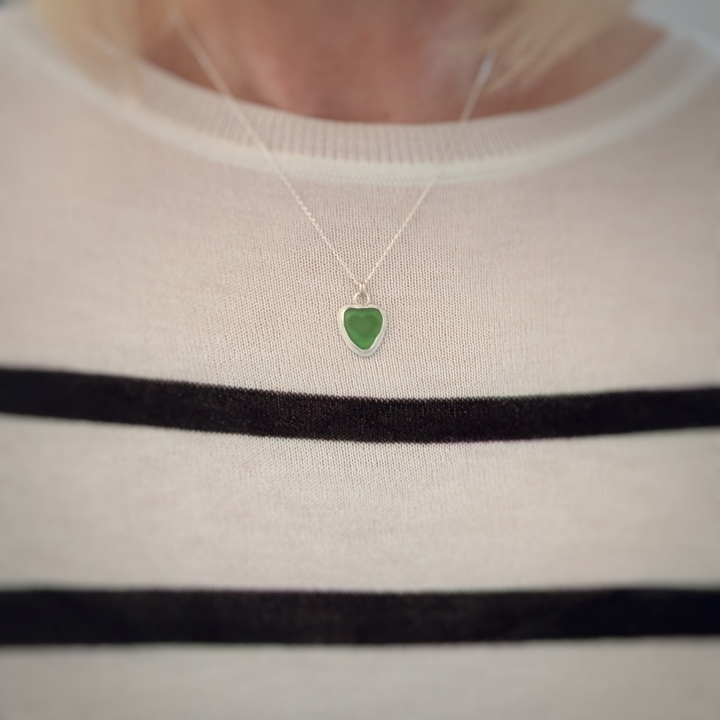 Model in stripey top wearing Green Sea Glass silver pendant with heart shape cut out, with silver chain 