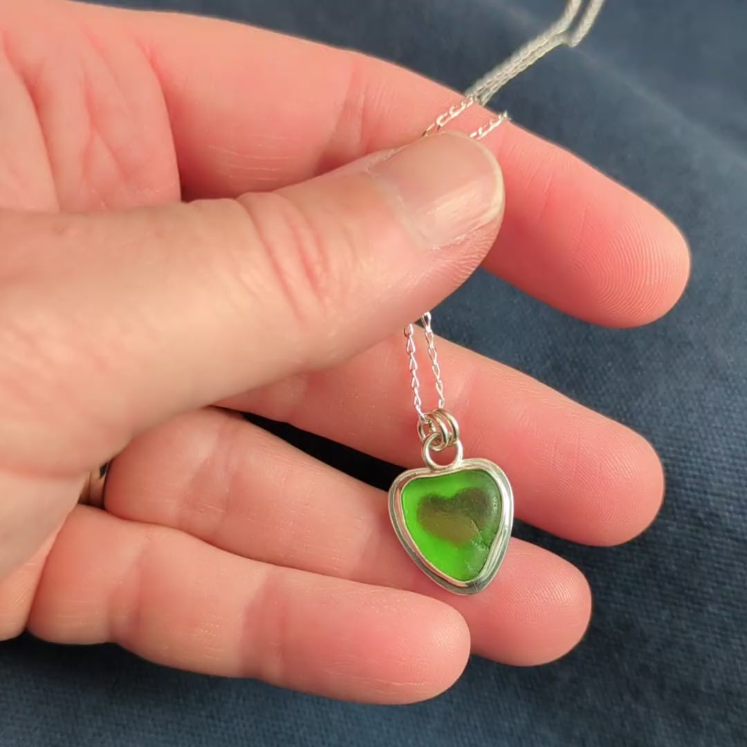 Video of hand holding Green Sea Glass silver pendant with heart shape cut out, with silver chain 