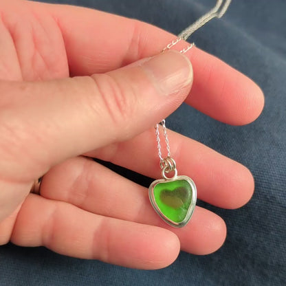 Video of hand holding Green Sea Glass silver pendant with heart shape cut out, with silver chain 