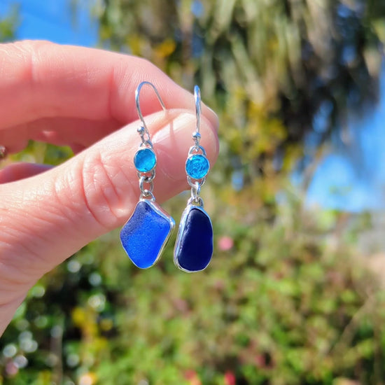 Hand holding dangly blue sea glass and apatite recycled silver asymmetrical earrings
