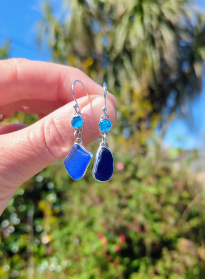 Hand holding dangly blue sea glass and apatite recycled silver asymmetrical earrings
