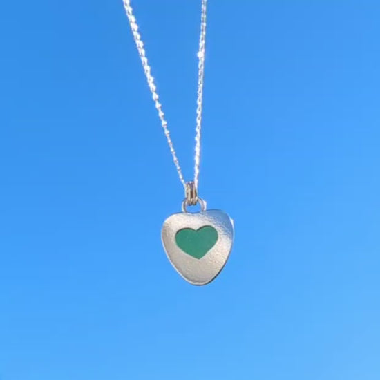 Video of Green Sea Glass silver pendant with heart shape cut out, with silver chain hanging with blue sky background.