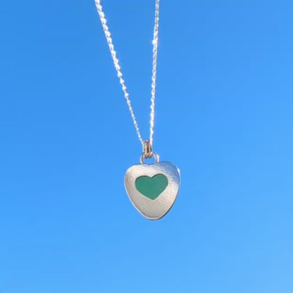 Video of Green Sea Glass silver pendant with heart shape cut out, with silver chain hanging with blue sky background.